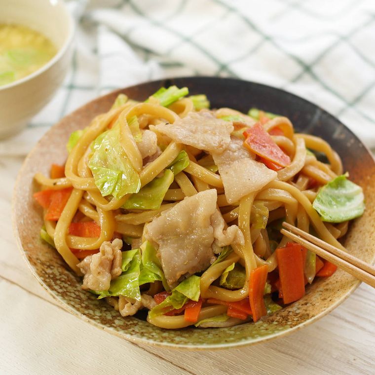 黄土色の皿に盛り付けられた豚肉とキャベツの焼きうどん