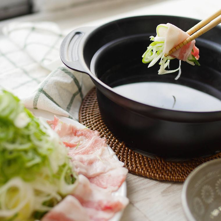 鍋にネギと豚肉を入れようとしている