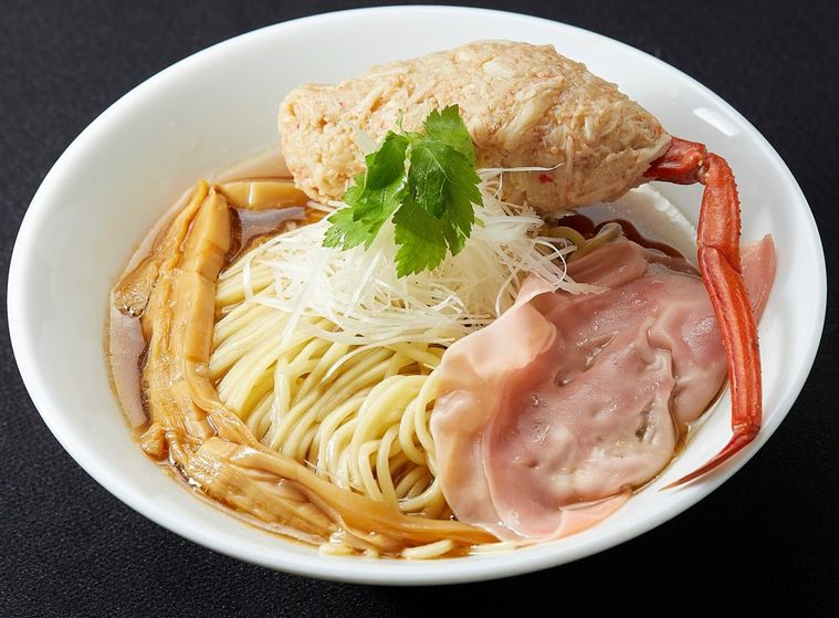 どんぶりの中に蟹の足とメンマ、焼豚がのった醤油ラーメンが入って置いてある