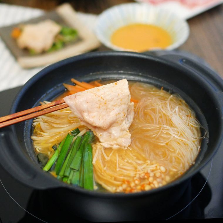 黒い鍋に入ったコチュジャン味噌のピリ辛しゃぶしゃぶの豚肉を箸でつかんでいる様子
