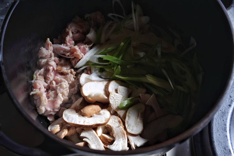 鍋で炒められた豚肉、しいたけ、長ネギ