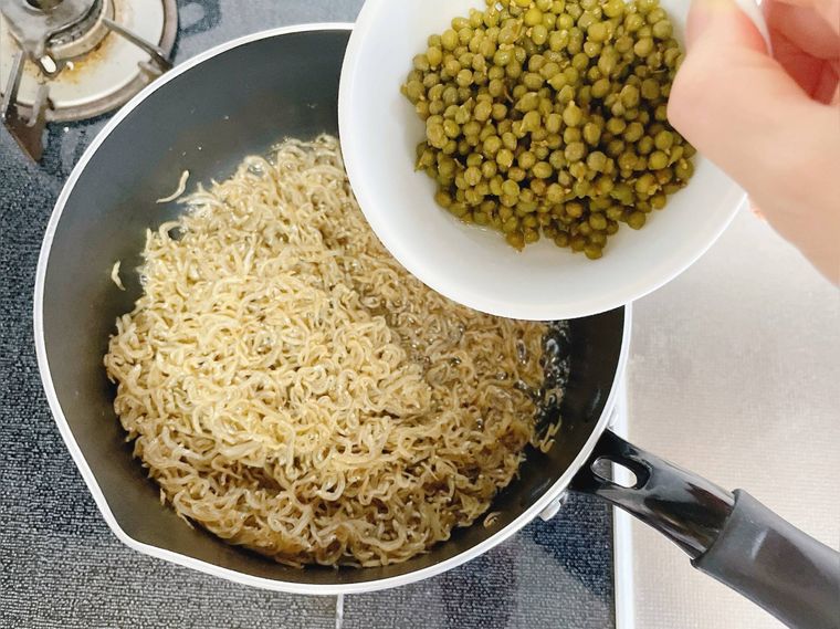 ちりめんじゃこを炊いている鍋に、山椒の塩漬けを入れる様子