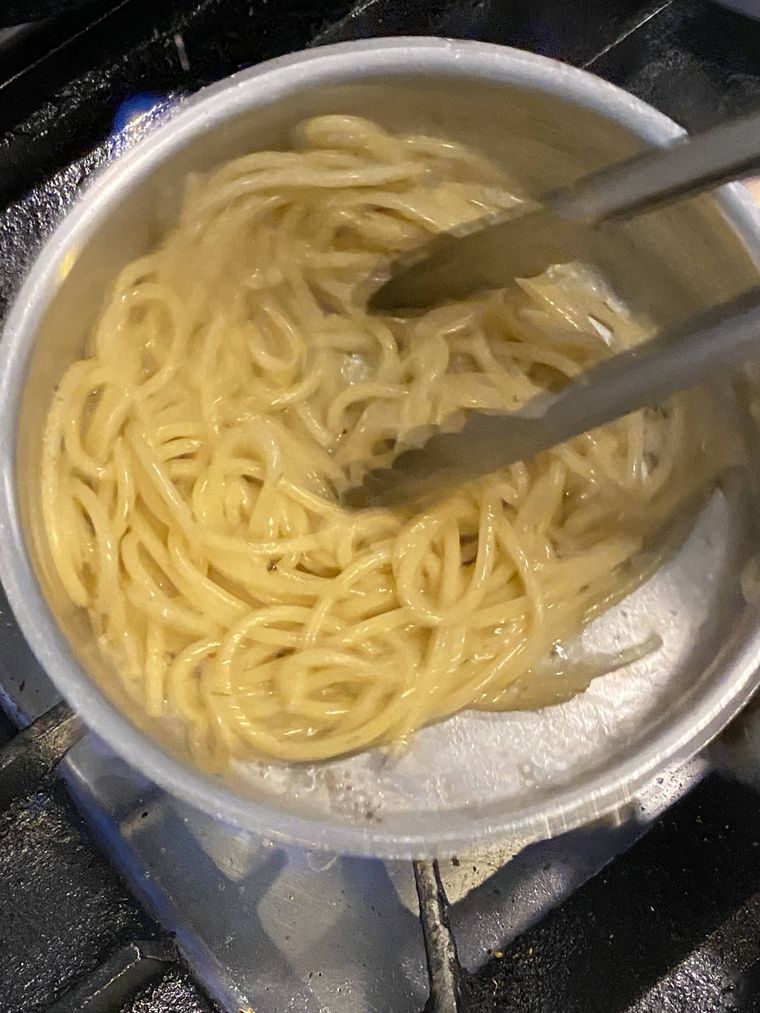 片手鍋でパターと胡椒で作ったソースをパスタにからめている