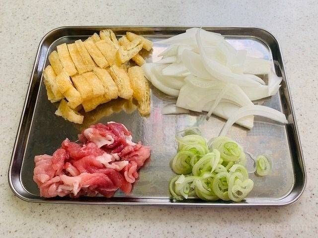 カットした玉ねぎ、油揚げ、豚小間肉、長ネギが並ぶ金属バット