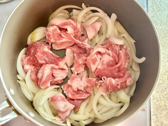 小鍋で炒めている玉ねぎに豚肩ロース肉を加える様子