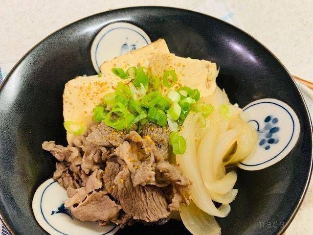 七味をふって青ネギを散らした、肉豆腐の盛られた黒い小鉢