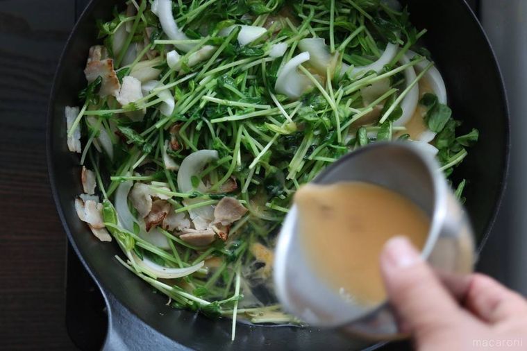 溶き卵が注がれている豆苗、玉ねぎ、ベーコンが入っているフライパン