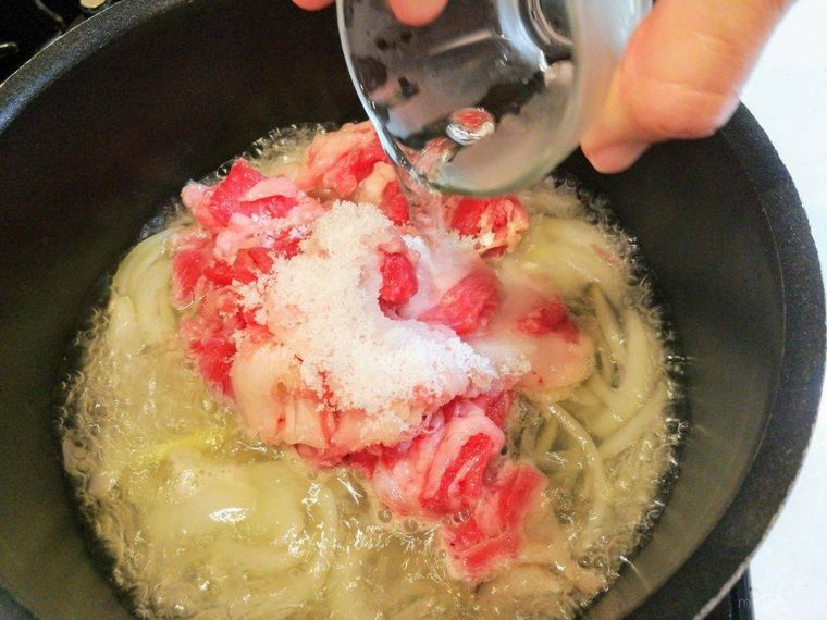 煮込んだたまねぎに牛肉と調味料を加える様子