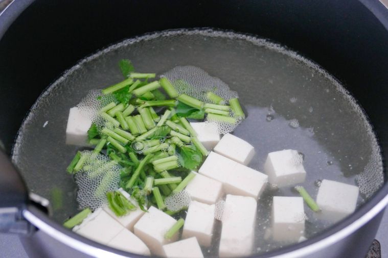 モロヘイヤの茎と豆腐を鍋で煮る様子