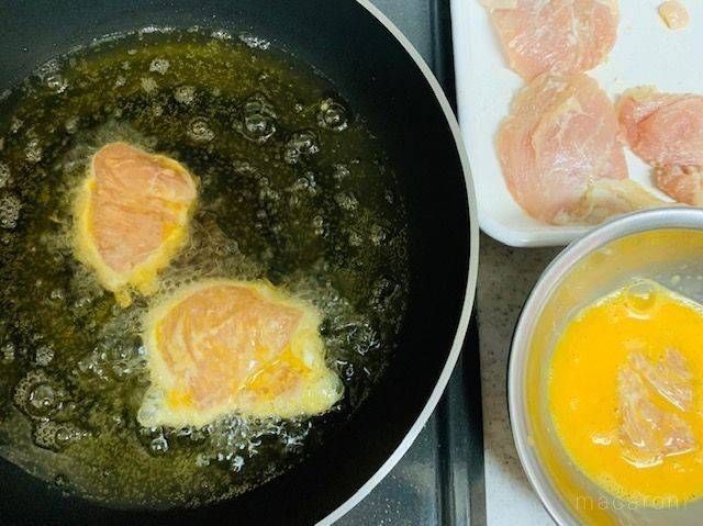 溶き卵をつけ、少なめの油で揚げ焼きしている鶏むね肉が入ったフライパン