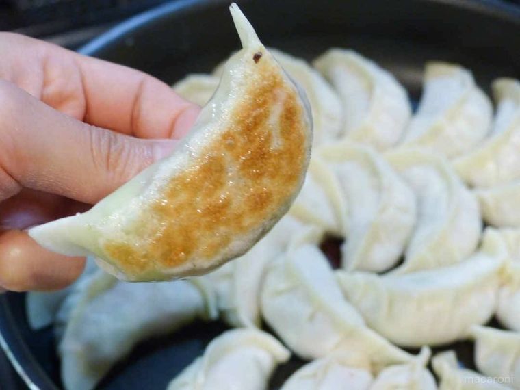 餃子を手でつまんで裏面の焼き色をチェックする