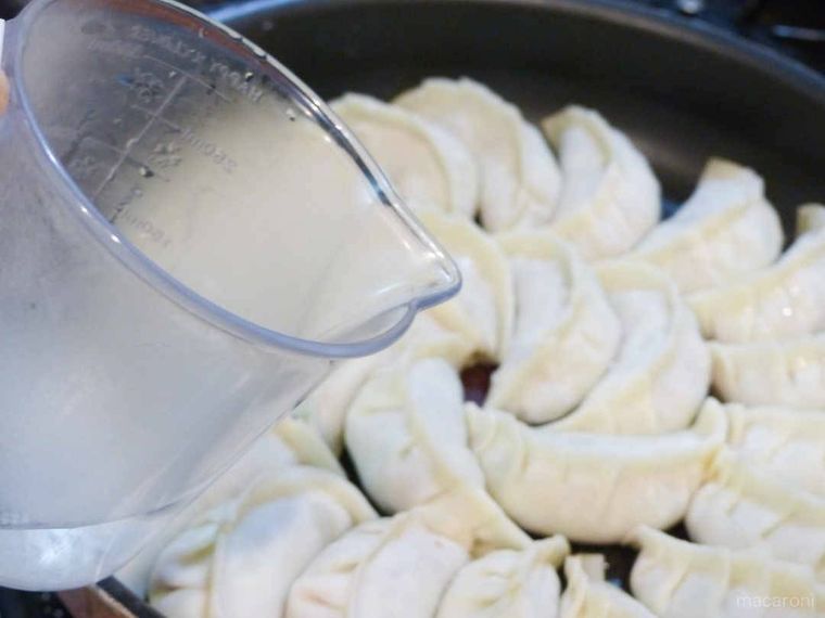 餃子の並んだフライパンに計量カップで熱湯を注ぐ