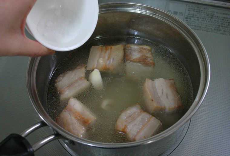 豚バラ肉を煮込んでいる鍋に調味料を入れている様子