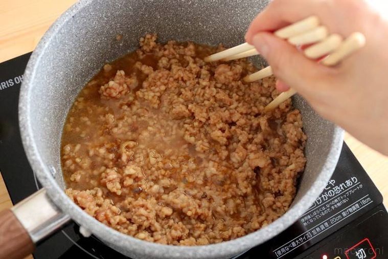 深い鍋に入った鶏ひき肉の材料を4本のお箸でかき混ぜているところ