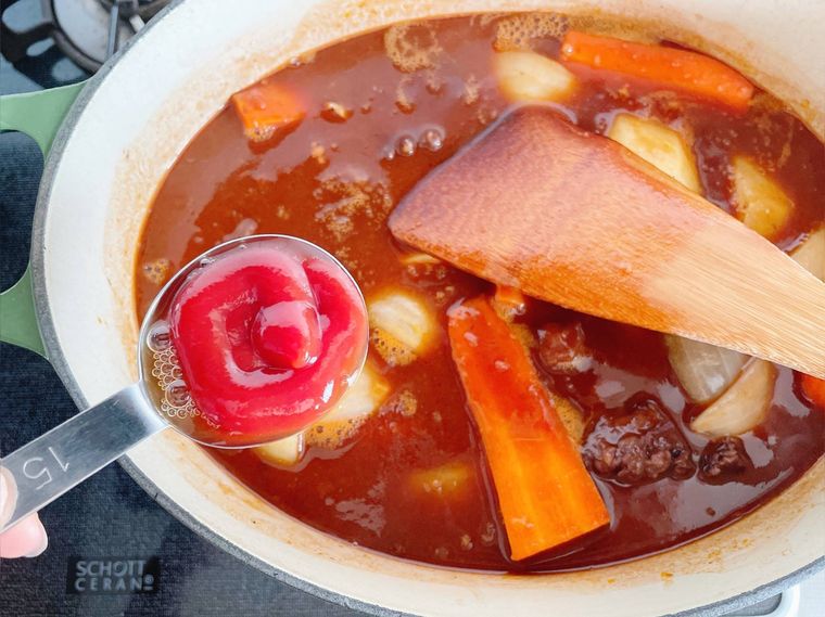 牛すじ肉と野菜を煮込む楕円の鍋にケチャップを入れる様子