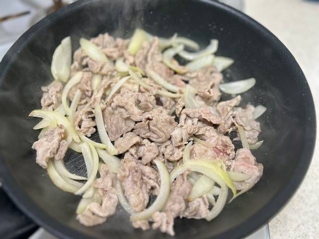 フライパンで豚こま肉と玉ねぎを炒め合わせている様子