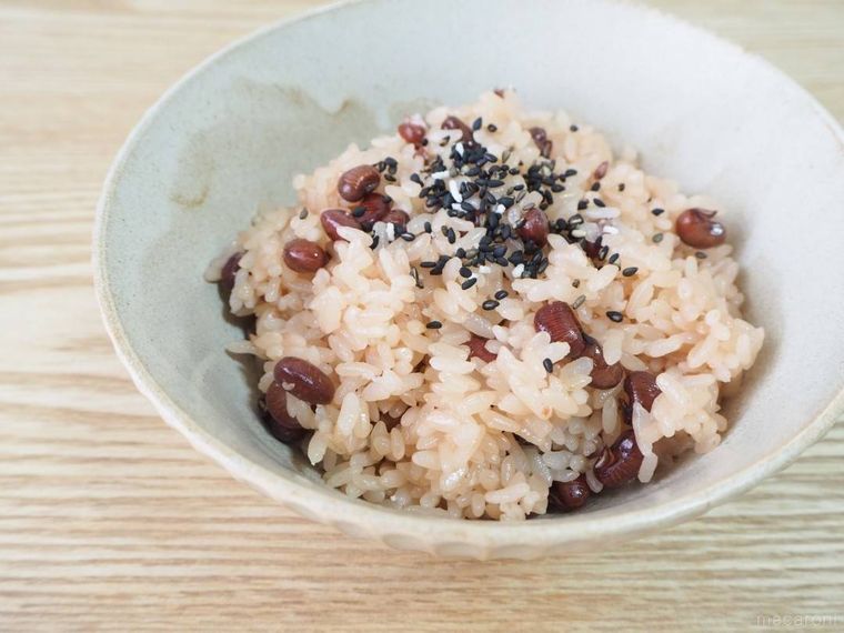 お茶碗に盛ったお赤飯の上にごま塩をかける様子