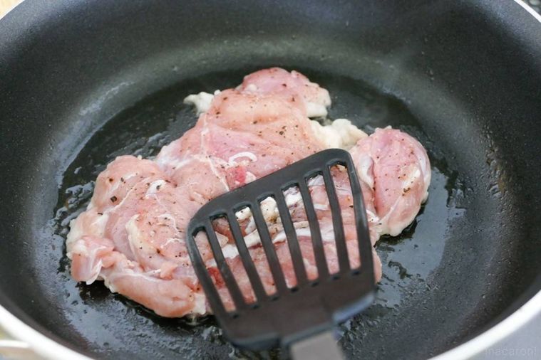 フライパンに入れた鶏肉をフライ返しで押し付けながら焼く様子