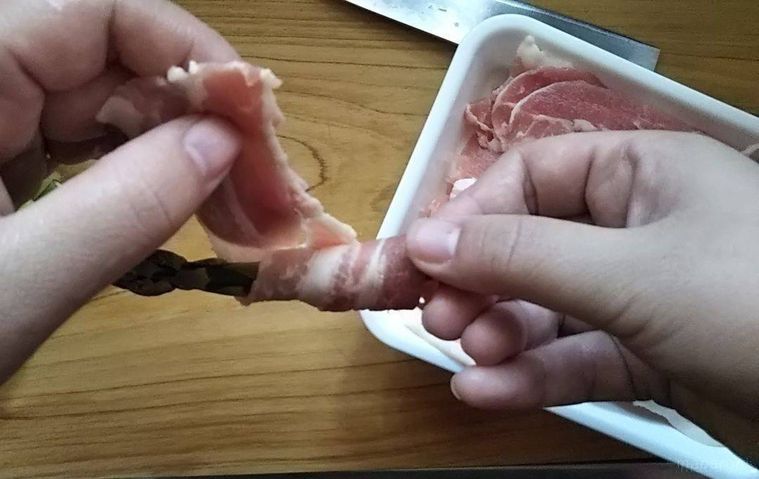 アスパラに豚バラ肉を巻いている手のアップ