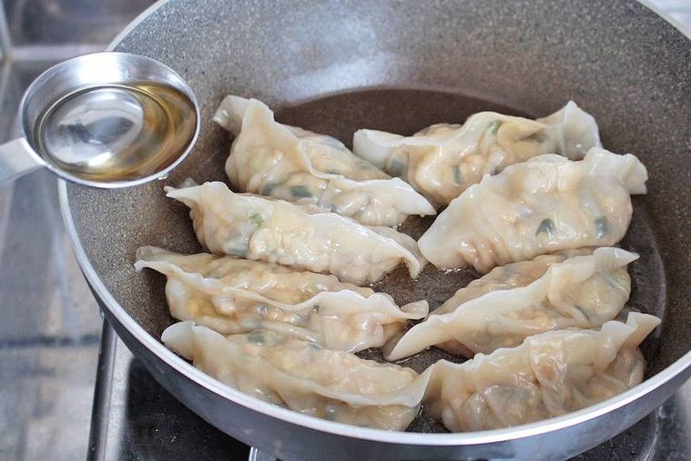 蒸しあがった餃子が並ぶフライパンにごま油を引くところ