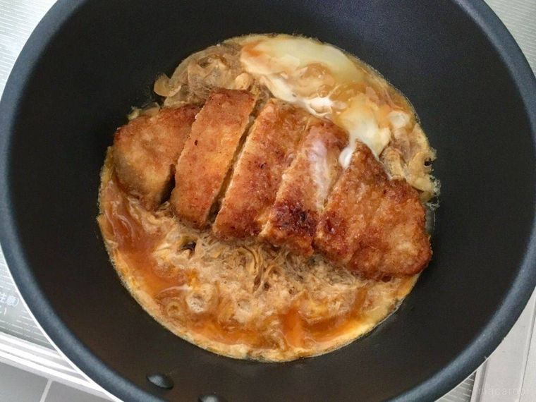 フライパンでとんかつと卵を半熟に煮ている様子