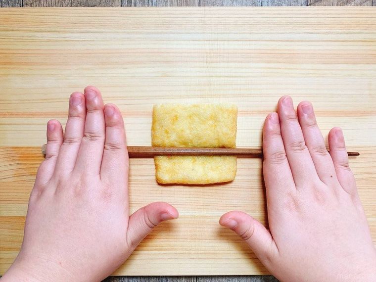木のまな板にのせた油揚げの上で、菜箸を転がしている様子