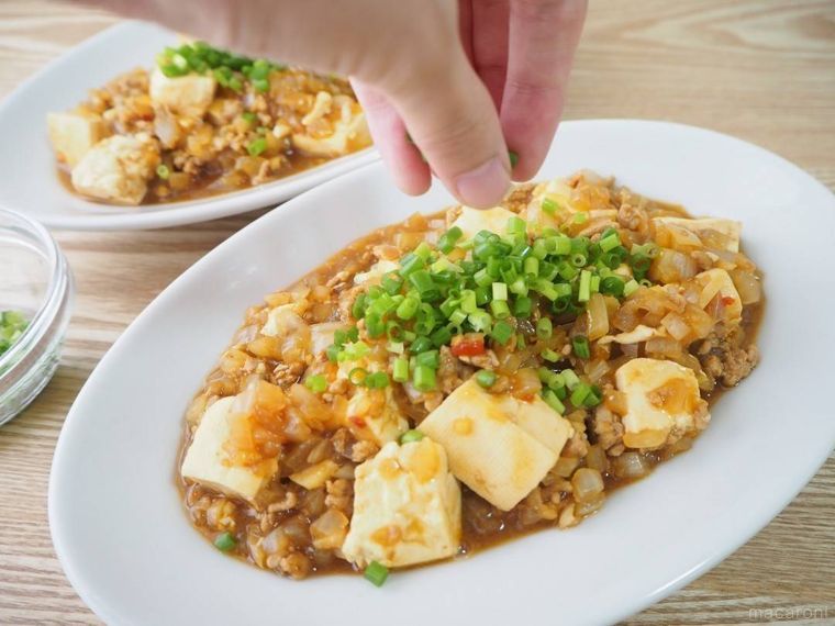 お皿に盛った麻婆豆腐に小口ねぎを振りかける様子