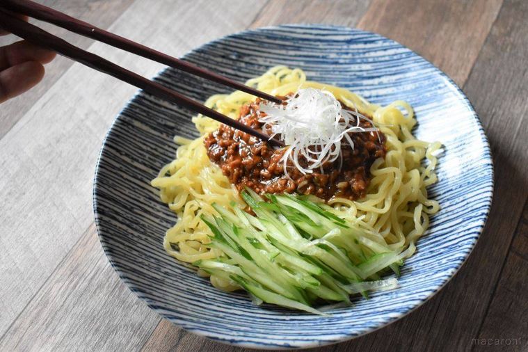 皿に麺、きゅうり、肉味噌、白髪ねぎを盛り付けているところ