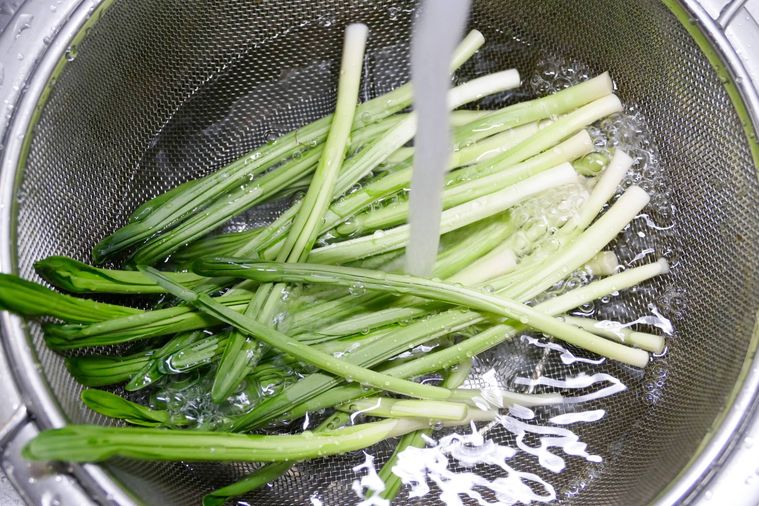 行者にんにくをザルに入れて流水で洗う様子