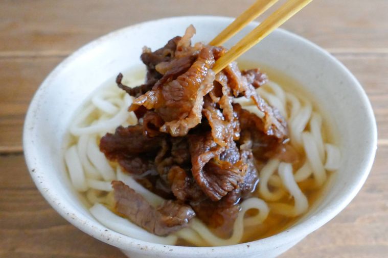 うどんの入っている丼に煮た牛こま肉をのせる様子