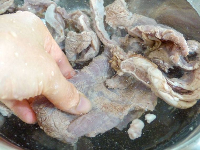 水を張ったボウルで牛すじ肉を手で洗う様子