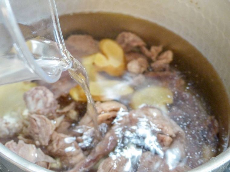 牛すじ肉としょうが、水が入った鍋に酒を加える様子