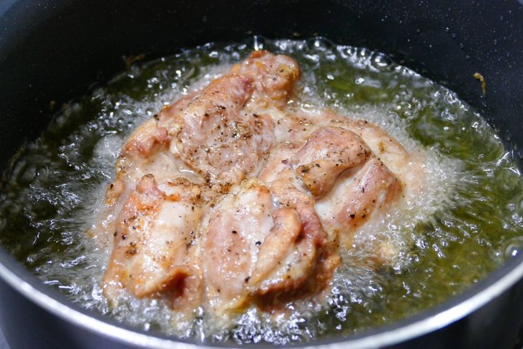 色づいた鶏もも肉を油鍋で揚げる様子