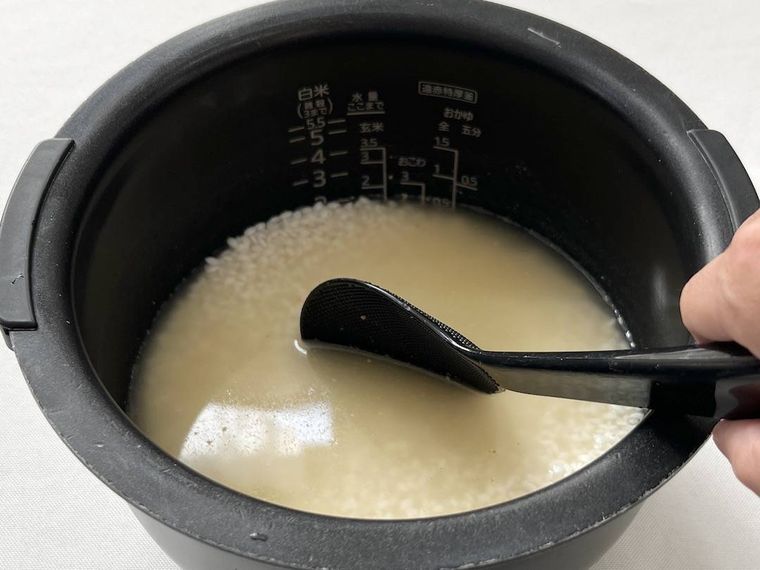 米、調味料、水が入った炊飯釜をしゃもじでかき混ぜている