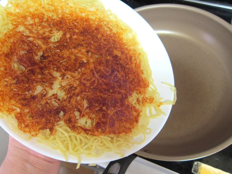 白い皿の焼いた焼きそば麺をフライパンに戻すところ