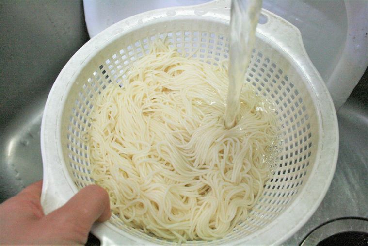 ザルに上げたそうめんを流水で洗っている様子