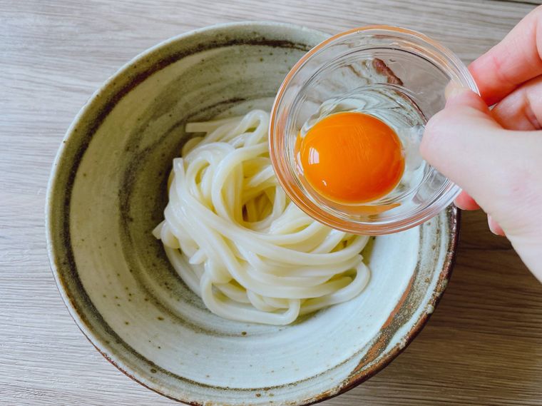 うどんに卵黄をのせる様子