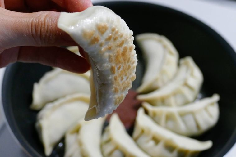 薄い焼き色がついた餃子を手でつまみ上げる様子