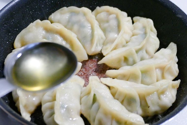 蒸し終えた餃子に油をまわしかける様子