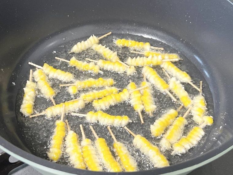 つまようじが刺さったとうもろこしを揚げ焼きにしている様子