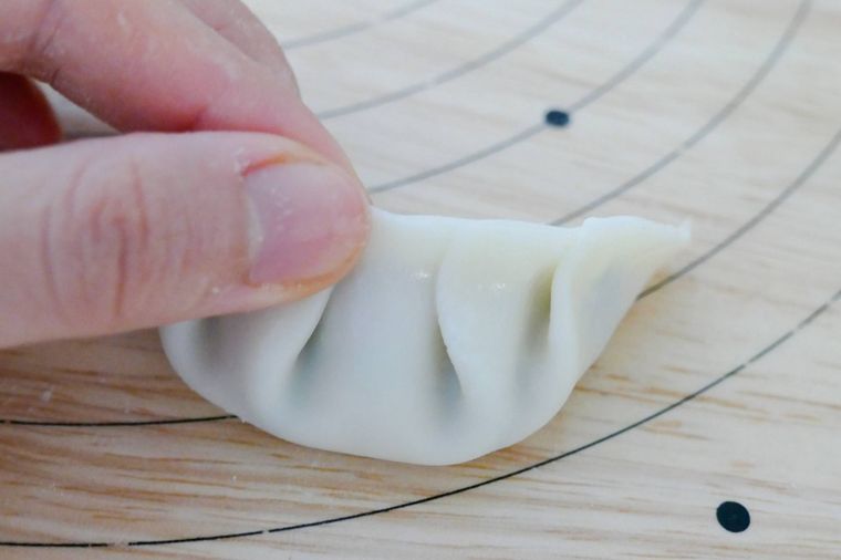 餃子の皮のふちを指でつまんで閉じる様子