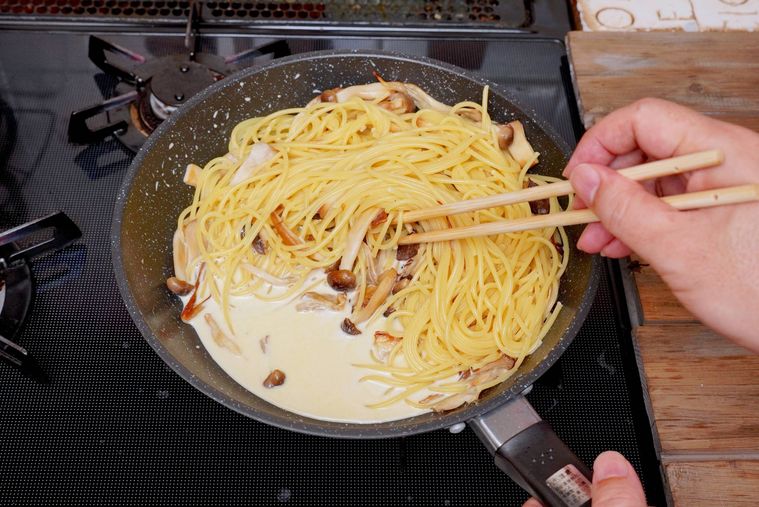 フライパンできのこクリームソースとパスタを和えている