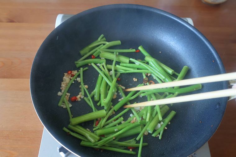 フライパンでにんにく、唐辛子、空芯菜の茎を炒めている