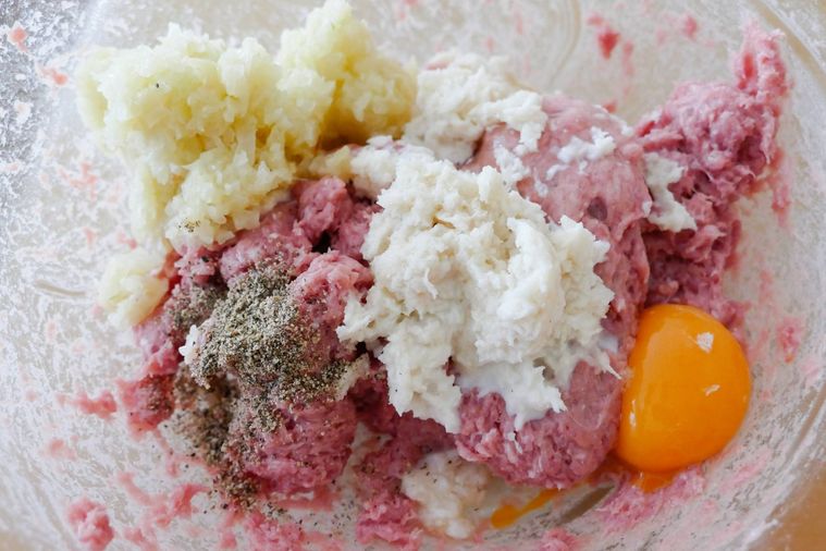 合い挽き肉が入っているボウルに炒めた玉ねぎやパン粉、卵などを加えた様子