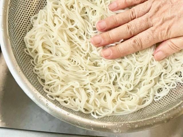 手で押さえながら水気を切っているザルに入ったそうめん