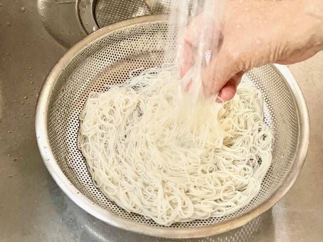 ゆでたそうめんをザルにあげて流水で洗っている様子