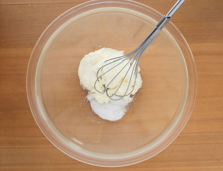 ボウルに入ったクリームチーズに、砂糖を加えて泡立て器で混ぜる様子
