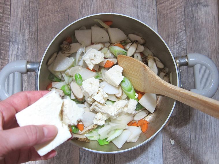 鍋に木綿豆腐を手でちぎって入れているところ