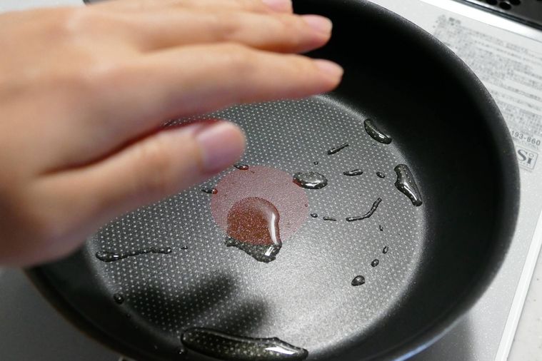 フライパンにサラダ油を入れて温め、手をかざして温度を確かめる様子
