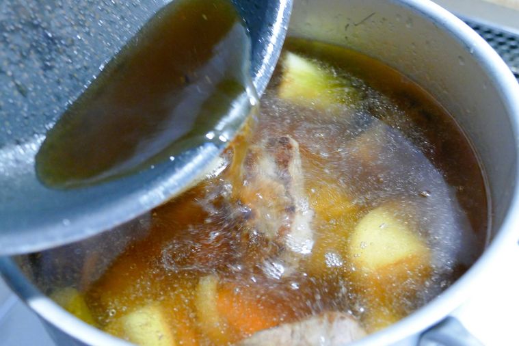 牛すね肉と野菜が入っている鍋に、フライパンに入れた水を加える様子